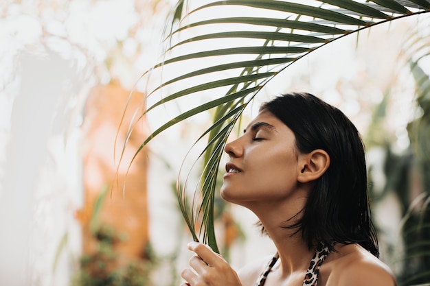 Free photo happy caucasian woman posing at exotic resort. outdoor shot of blithesome woman sniffing palm tree.