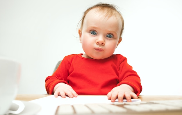 Happy child baby girl sitting with keyboard of modern computer or laptop in white studio