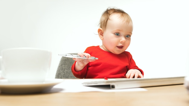 Happy child baby girl sitting with pen and keyboard of modern computer or laptop isolated on a white studio