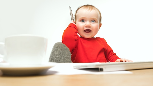 Happy child baby girl sitting with pen and keyboard of modern computer or laptop isolated on a white studio