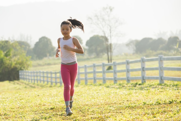 Free photo happy child girl running on meadow in summer in nature. warm sunlight flare. asian little is running in a park. outdoor sports and fitness, exercise and competition learning for kid development.