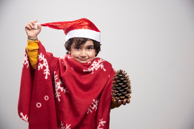 Happy child in red uniform and hat holding pinecone