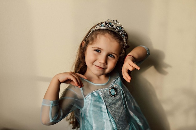 Free photo happy child with long wavy hair posing at camera with happy true emotions studio portrait of little birthday girl wears cute holiday dress and crown