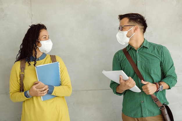 Free Photo happy college students wearing protective face masks while standing by the wall and talking.