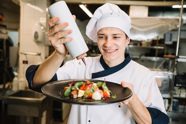 Happy cook pouring sauce on plate with salad