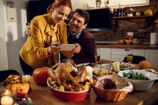 Happy couple celebrating Thanksgiving and taking picture of dining table set for dinner