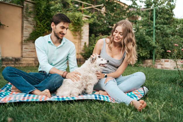 Happy couple of guys playing with their dog in the backyard on the grass. Cheerful old dog