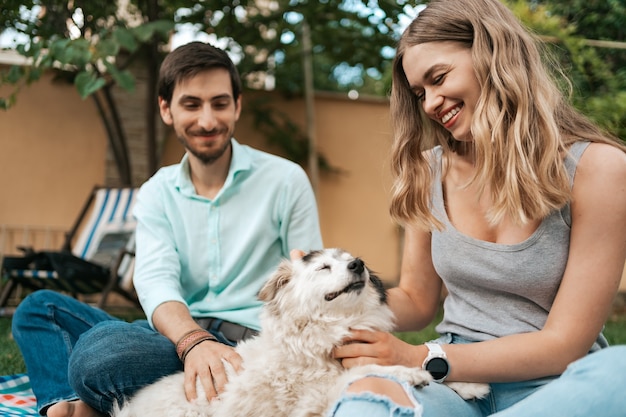 Happy couple of guys playing with their dog in the backyard on the grass. Cheerful old dog