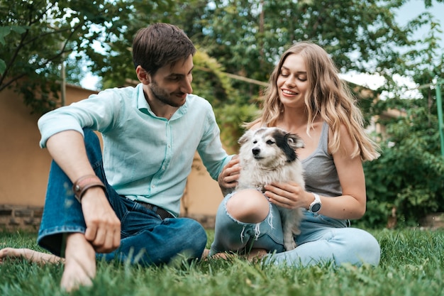 Happy couple of guys playing with their dog in the backyard on the grass. Cheerful old dog