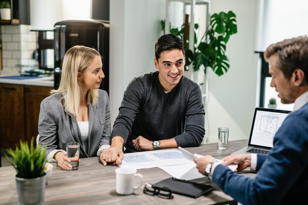 Happy couple holding hands while talking about housing plans with real estate agent at home