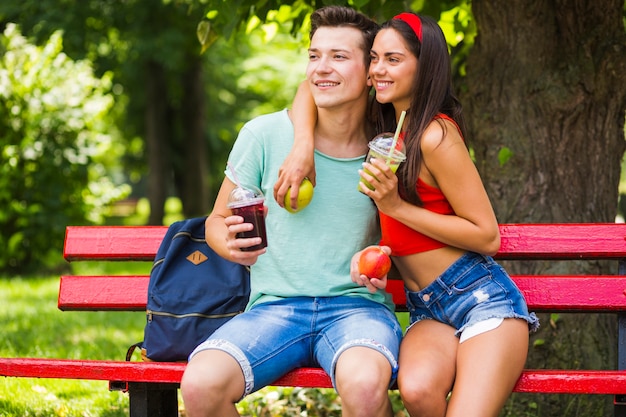 Free photo happy couple holding healthy fruit and smoothies enjoying in the park