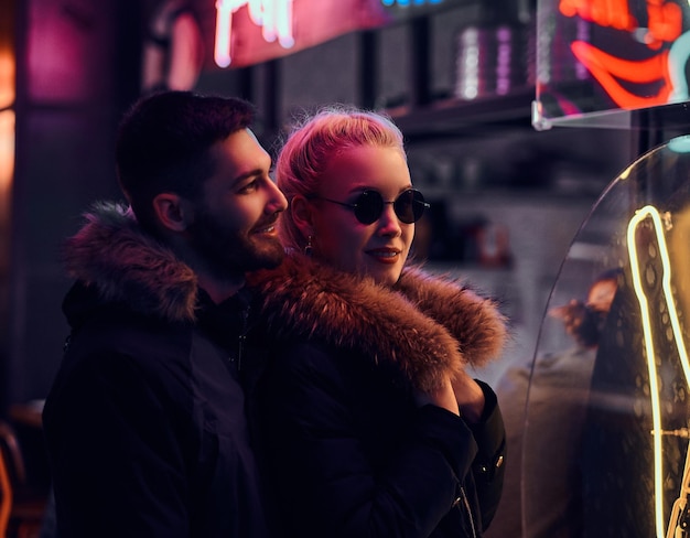 Free Photo happy couple in love. a beautiful girl and handsome man standing in the night on the street. illuminated signboards, neon, lights.