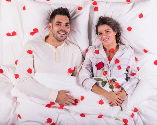 Happy couple lying in bed with rose petals 