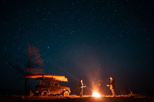 Free photo happy couple man and woman standing in front burning bonfire