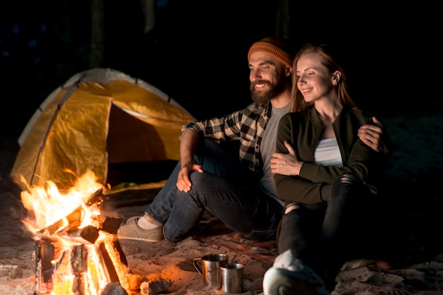 Free photo happy couple sitting together by bonfire