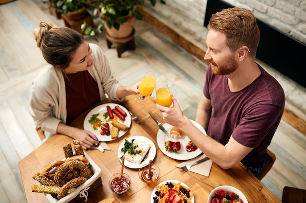 Happy couple toasting with orange juice during breakfast at home