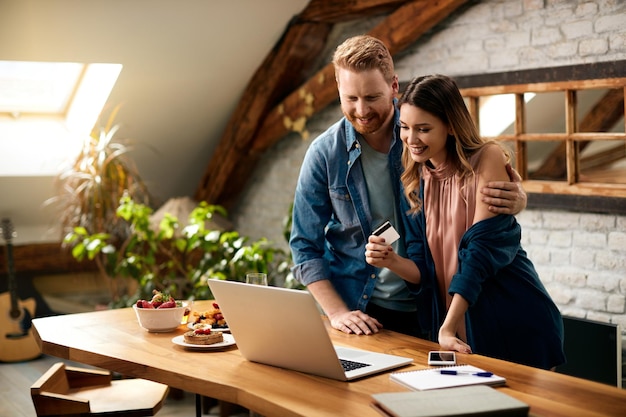 Happy couple using laptop and credit card while shopping online at home