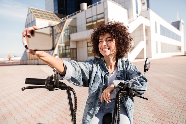 Happy curly woman sitting on modern motorbike outdoors