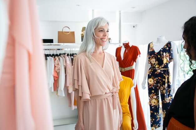 Happy customer trying on new dress in boutique. Woman choosing clothes in fashion store. Buying clothes in boutique concept