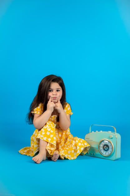 Happy cute baby girl fashionable yellow baby clothes posing studio on blue background