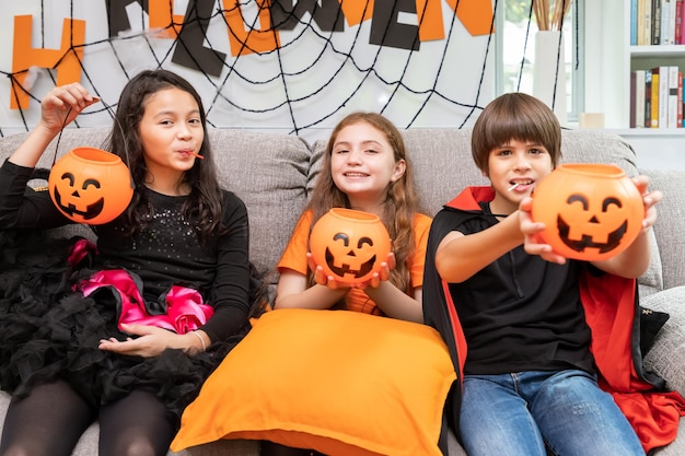 Free photo happy cute children boy and girls in costume on sofa in living room during halloween party holding pumpkin jacko'lantern in hand