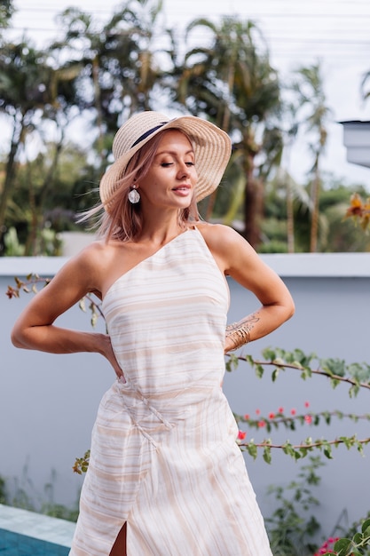 Happy cute romantic caucasian woman in elegant white open back dress and straw hat