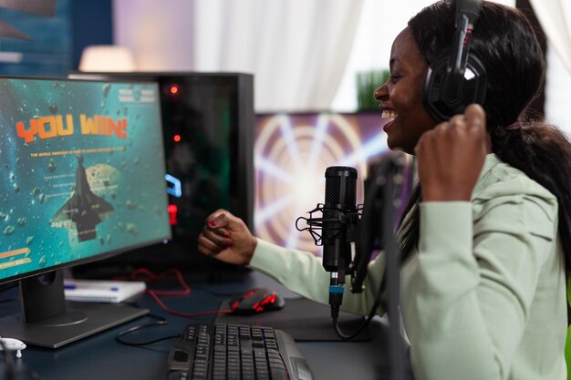 Happy cyber woman winner sitting at gaming desk playing esport videogames winning online championship. Successful pro gamer player streaming live using RGB computer equipment. entertainment lesiure