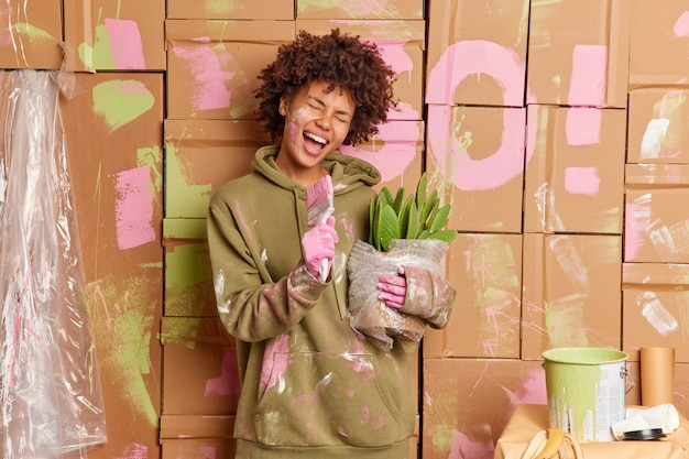 Free Photo happy dark skinned young woman does repairs in apartment has fun after painting walls sings in paint brush r