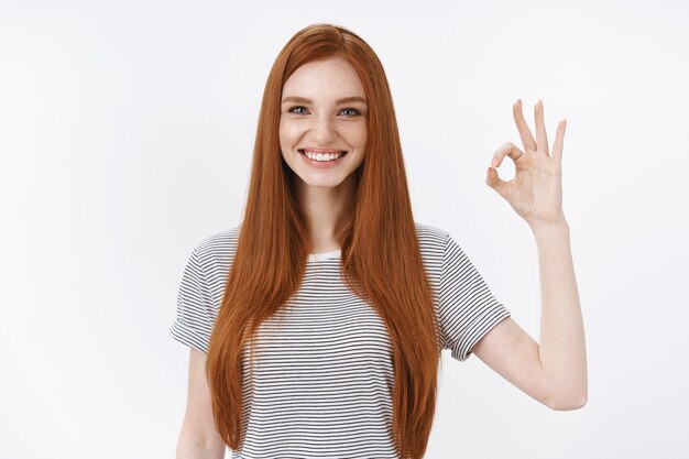 Happy delighted attractive redhead female student give positive reply show okay ok normal gesture express positive good attitiude like result, standing white wall