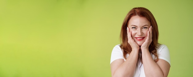 Free Photo happy delighted cheerful lucky redhead middleaged caucasian woman blushing joyfully receive touching cute gift touch cheeks pleased delighted smiling broadly feel happiness joy green background