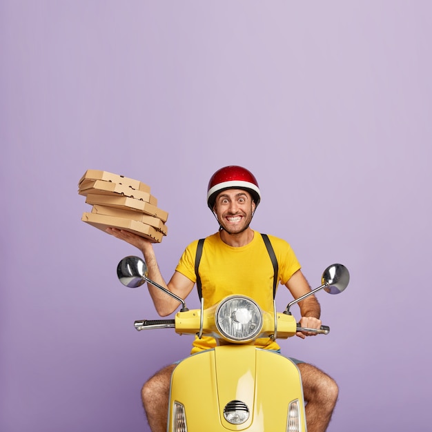 Free Photo happy deliveryman driving yellow scooter while holding pizza boxes