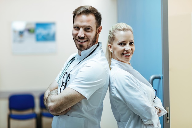 Free Photo happy doctor and his female colleague standing back to back with their arms crossed in the hospital and looking at camera