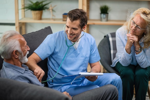 Free photo happy doctor listening heartbeat of mature patient while examining his during a home visit