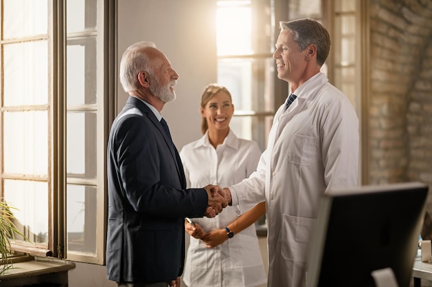 Free Photo happy doctor shaking hands with senior businessman while nurse is standing in the background