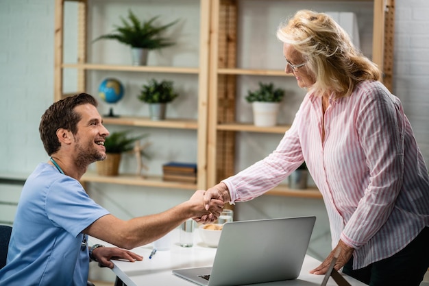 Free photo happy doctor shaking hands with senior woman who came to medical appointment