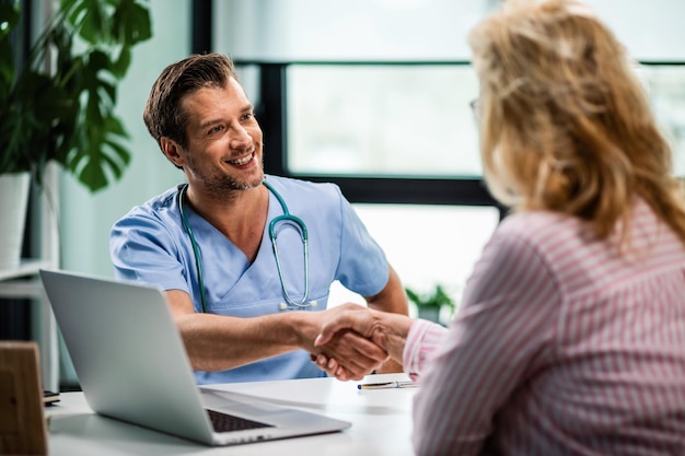 Free Photo happy doctor shaking hands with wife of his senior patient at medical clinic