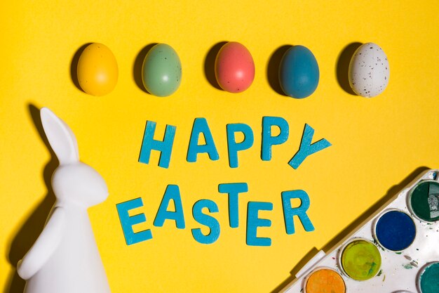 Happy Easter inscription with eggs and rabbit on table