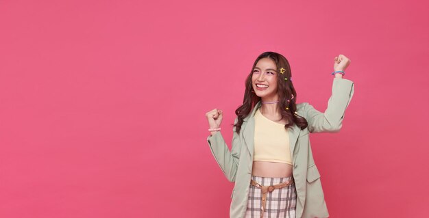 Happy ecstatic cheerful asian woman fist up raise win gesture isolated on pink copy space background