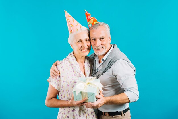 Happy elderly couple holding birthday gift on blue background