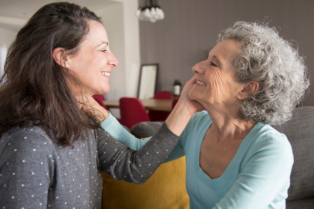 Happy elderly mother and daughter touching faces of each other