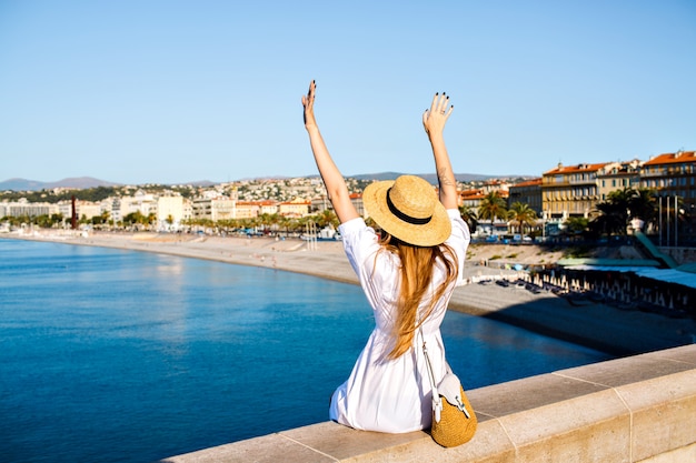 Happy elegant woman posing back, put her hand in the air and enjoying amazing view