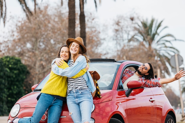 Happy embracing women near man leaning out from car 