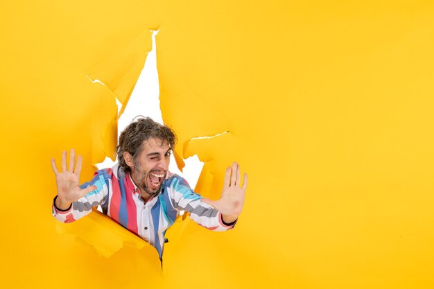 Happy and emotional young man showing ten in torn yellow paper hole background