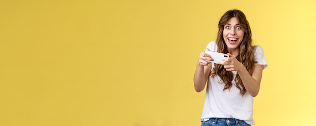 Free photo happy enthusiastic excited cute playful girl winning awesome smartphone game thrilled playing stare camera surprised triumphing smiling happily hold mobile phone horizontal yellow background