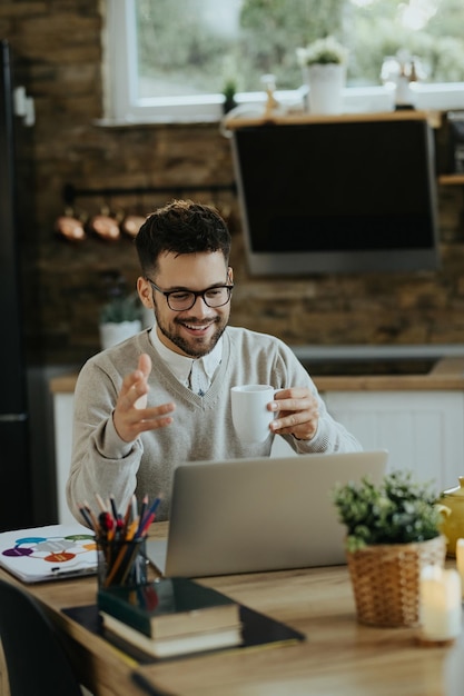 Happy entrepreneur drinking coffee during conference call over laptop at home