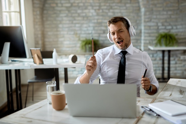 Happy entrepreneur having fun while listening music and singing in the office