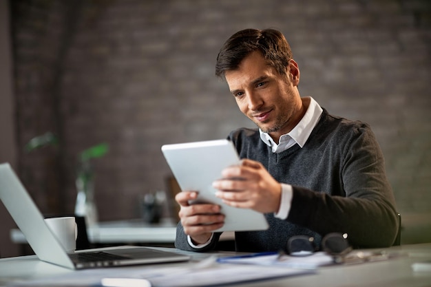 Happy entrepreneur using digital tablet and reading something while working in the office