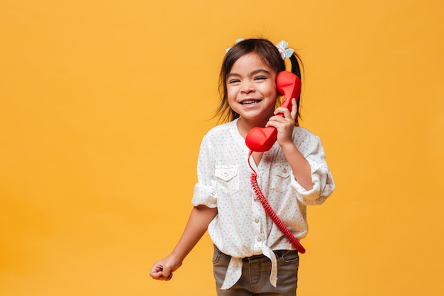 Happy excited little girl child talking by red retro telephone.