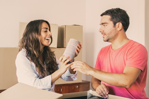 Happy excited young man and woman moving and unpacking things, getting out objects from open carton box