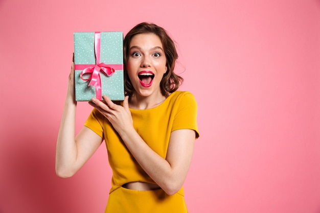 Happy exited pretty girl in yellow dress holding present, 